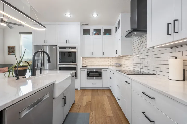 Modern kitchen featuring white cabinetry with black hardware, stainless steel appliances, a farmhouse sink, subway tile backsplash, and light wood-finish flooring