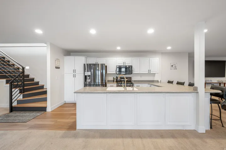 Open-concept kitchen featuring an expansive central island with a built-in sink, white cabinetry with contemporary hardware, stainless steel appliances, and recessed lighting