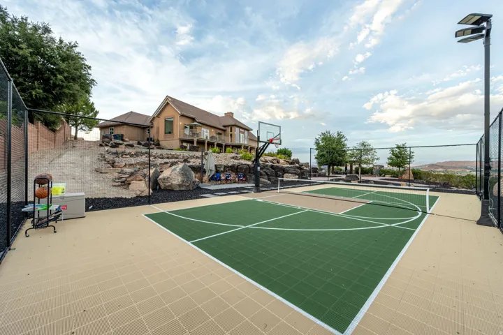 Multi-sport court with green and beige modular tile surfacing, basketball hoop, and tennis net