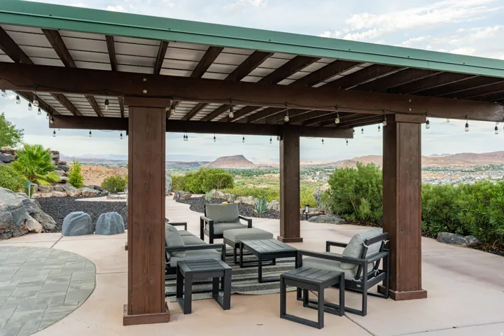 Expansive patio featuring a wood-finish pergola with string lighting, concrete flooring, and surrounding landscaping