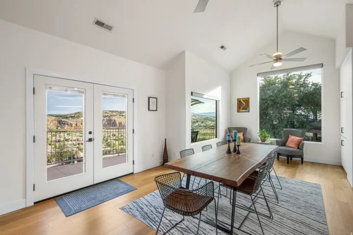 Spacious room featuring a vaulted ceiling with a ceiling fan, a large picture window, and a set of French doors