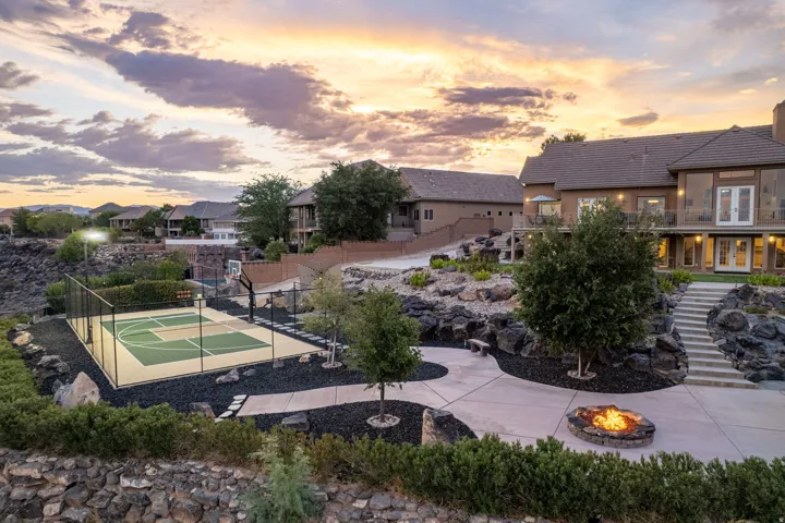 Expansive outdoor living area featuring a sport court, a built-in fire pit, multiple concrete patios, stone retaining walls, and mature landscaping