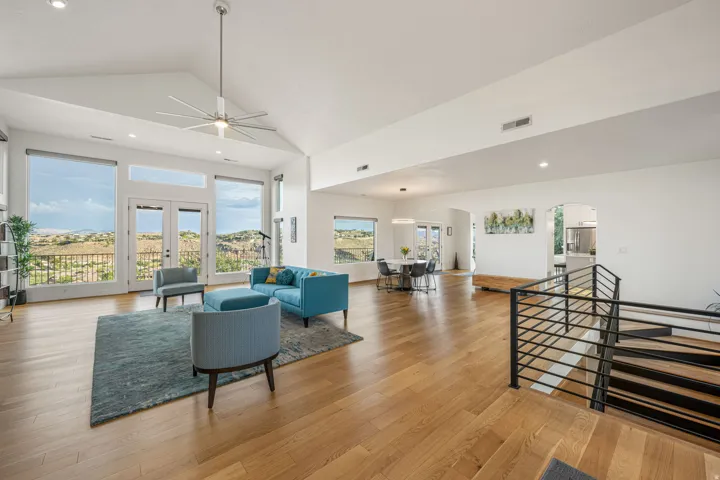 Open-concept living space featuring vaulted ceilings, wood-finish flooring, a contemporary ceiling fan, and multiple large windows with exterior access
