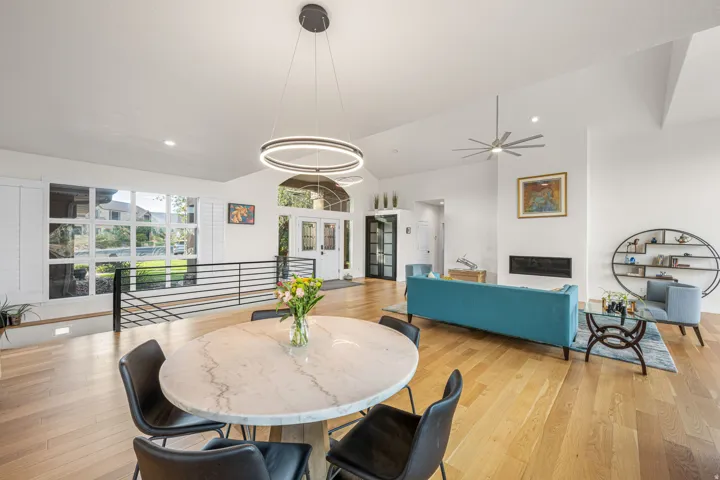 Expansive interior featuring high vaulted ceilings, light wood-finish flooring, a modern linear fireplace, a black metal staircase railing, and a contemporary chandelier
