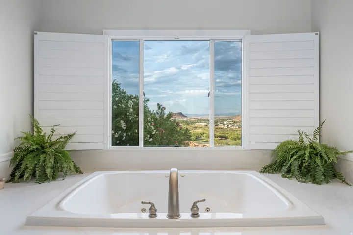 Soaking tub with brushed nickel fixtures, plantation shutters, and a surrounding countertop