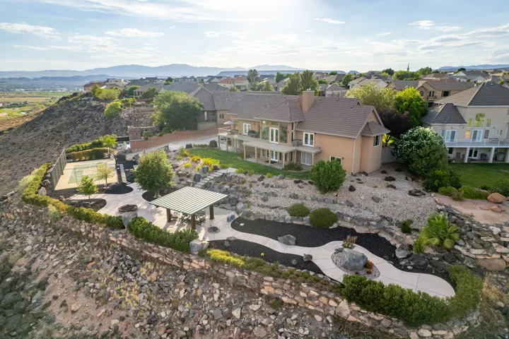 Expansive terraced property featuring a private tennis court, covered patio structure, and winding concrete pathways