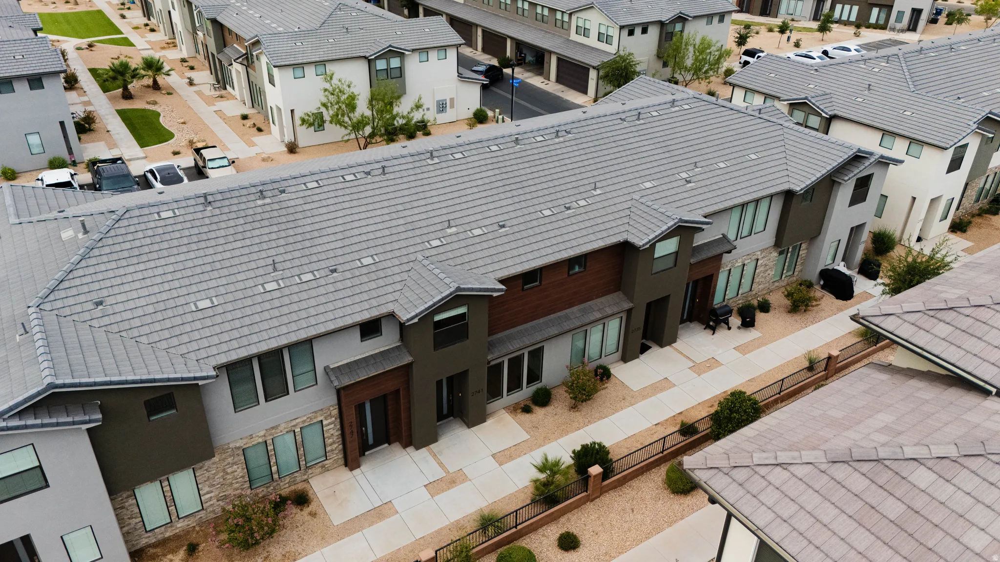 Modern multi-family residential building featuring a grey tile roof, contemporary exterior finishes with stone accents, a landscaped front walkway, and private entryways