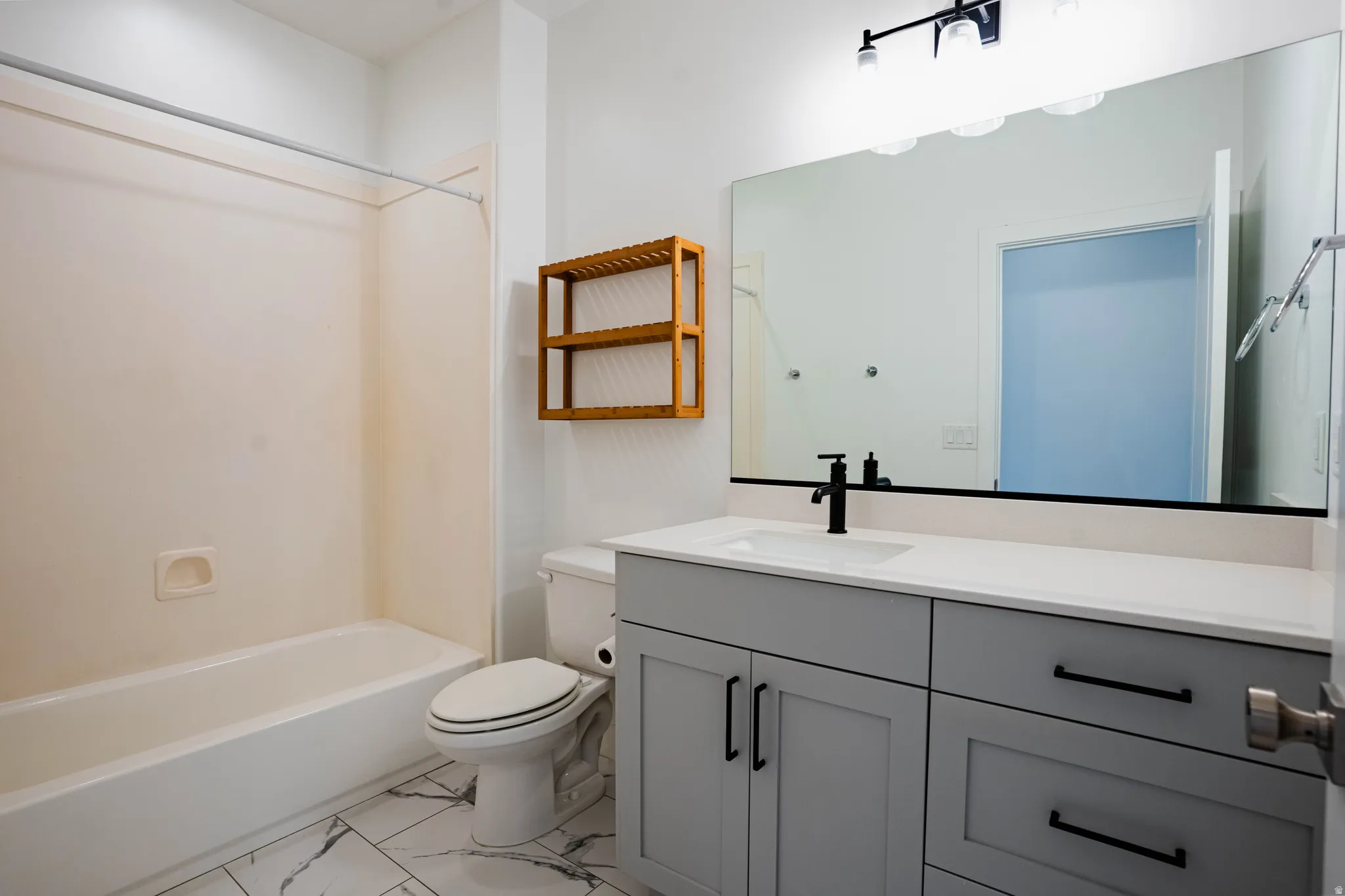 Well-appointed bathroom featuring a single vanity with gray cabinetry and black hardware, a white countertop, and a large wall-mounted mirror with an overhead light fixture