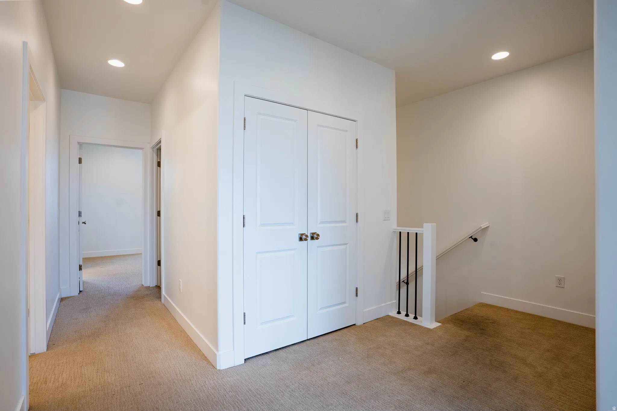 Hallway with light beige carpet flooring, recessed lighting, white walls, and white baseboards