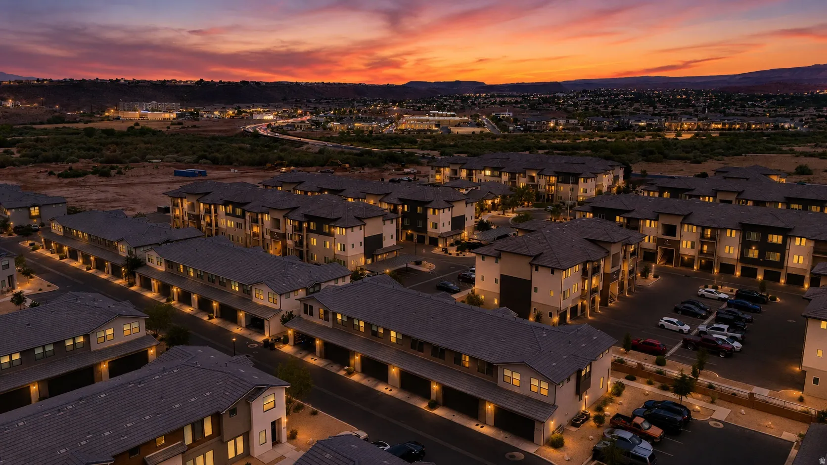 Modern multi-story residential complex featuring contemporary architecture, integrated garages, street-level parking, and exterior lighting