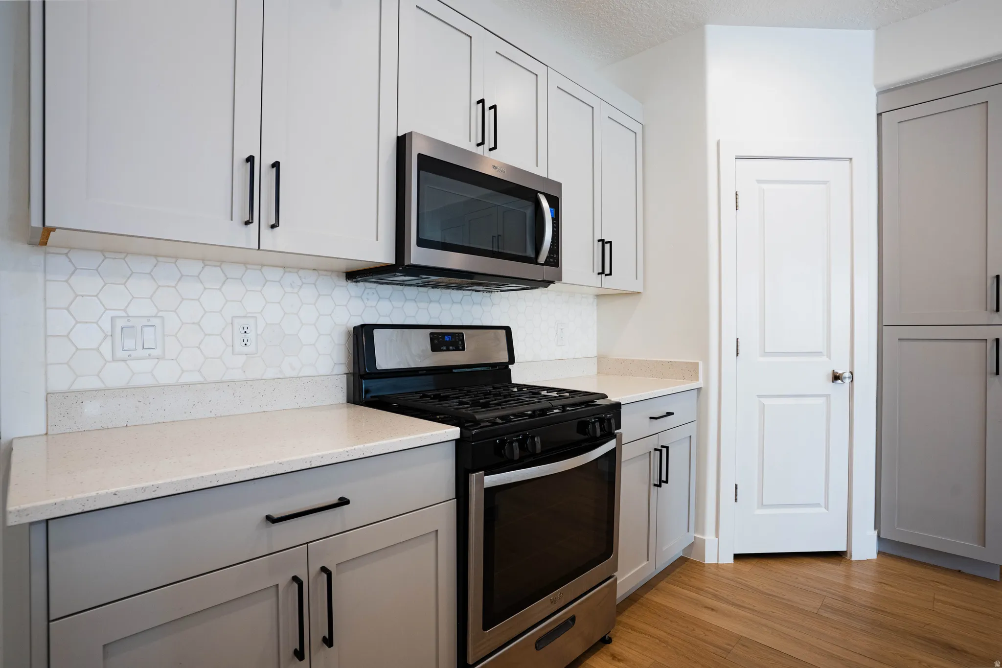 Kitchen featuring light gray shaker cabinetry with matte black hardware, stainless steel appliances, speckled countertops, and a white hexagonal tile backsplash