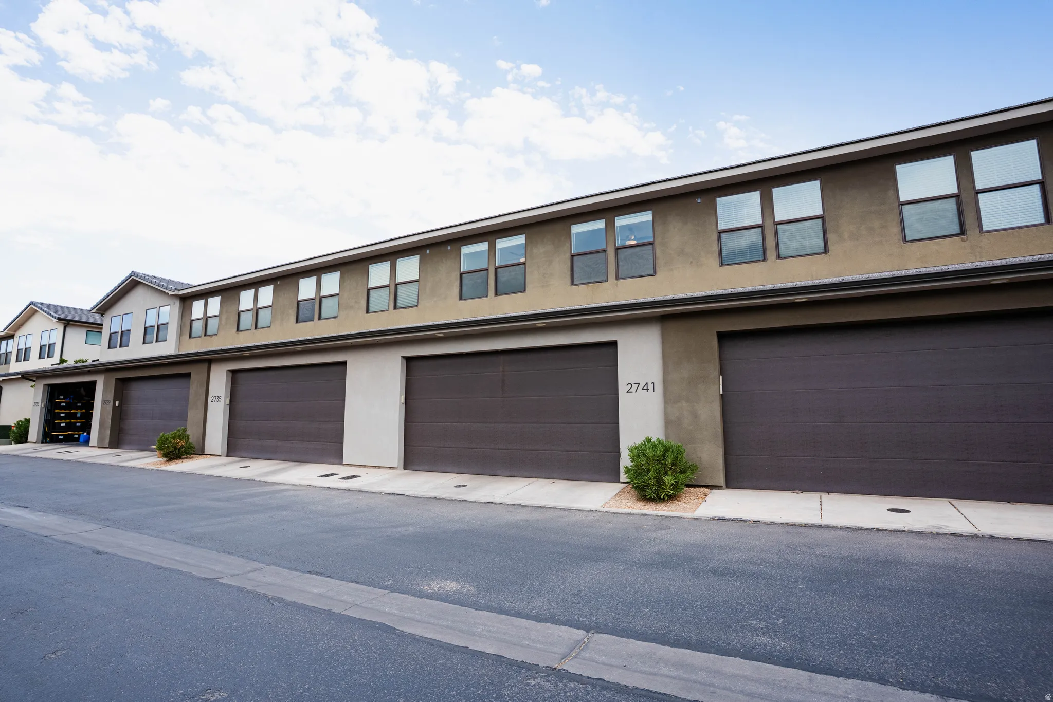 Contemporary multi-story facade featuring stucco exterior, numerous windows with dark frames, multiple garage doors, and a paved driveway