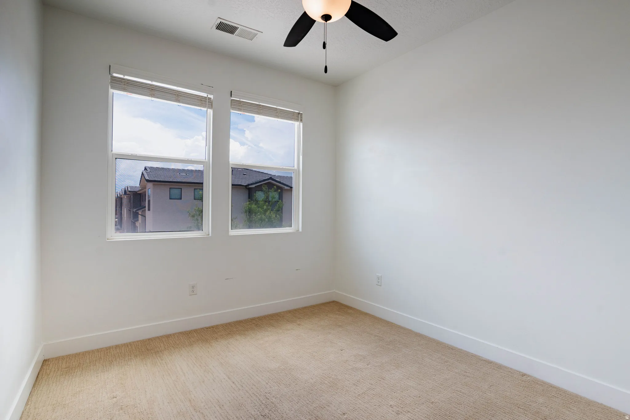 White-painted interior room featuring two windows, neutral carpeting, a ceiling fan with integrated lighting, and white baseboards