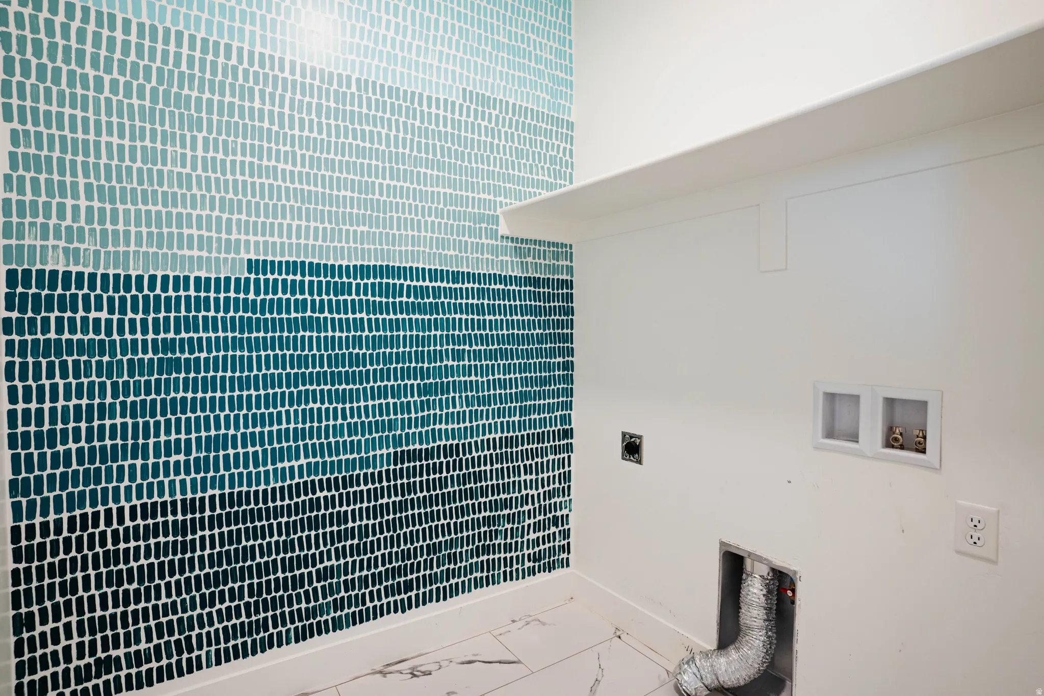 Laundry area featuring a multi-toned blue mosaic tile accent wall, white wall shelving, white electrical outlets, and a floor with a light-colored marble-look pattern