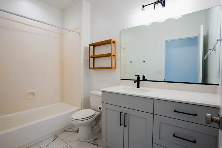 Well-appointed bathroom featuring a single vanity with gray cabinetry and black hardware, a white countertop, and a large wall-mounted mirror with an overhead light fixture