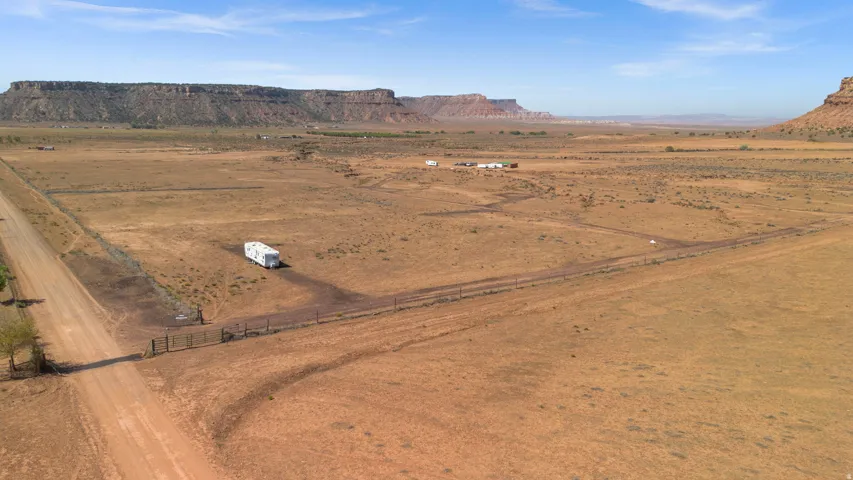 Expansive land parcel featuring a dirt road, partial fencing, and distant mesa formations