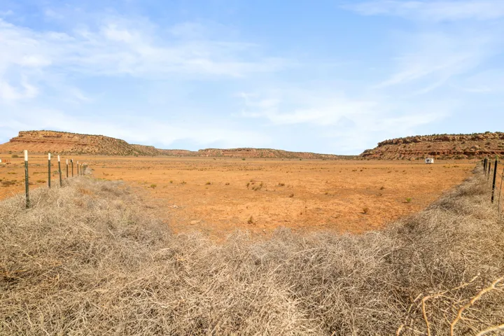 Expansive arid land parcel featuring a wire fence line, distant mesa formations, and a clear sky overhead