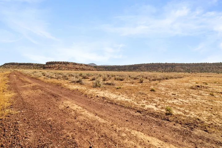 Expansive undeveloped land featuring a reddish-brown dirt path, scattered low-lying vegetation, and distant natural rock formations