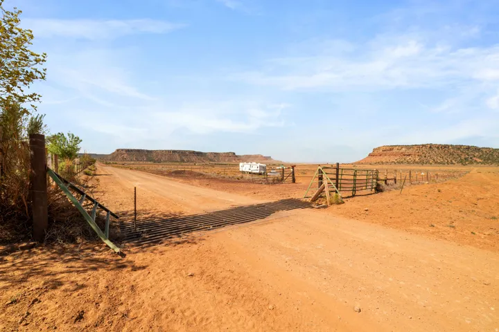 Expansive dirt road entrance with cattle guard and fencing, featuring a natural landscape with distant mesas under a clear sky