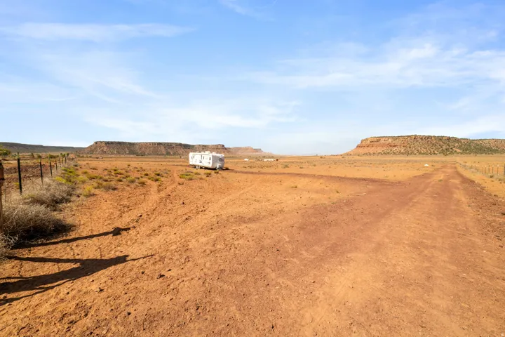 Expansive open land featuring a dirt road, sparse vegetation, and distant mesas