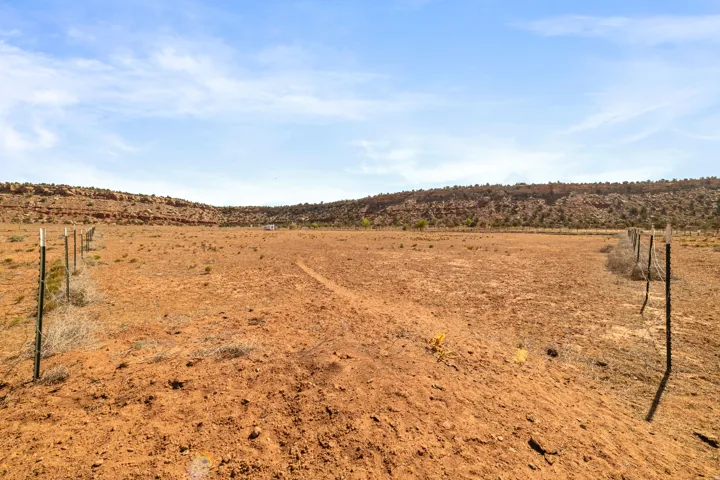 Expansive open land with natural red earth and sparse vegetation, bordered by fencing
