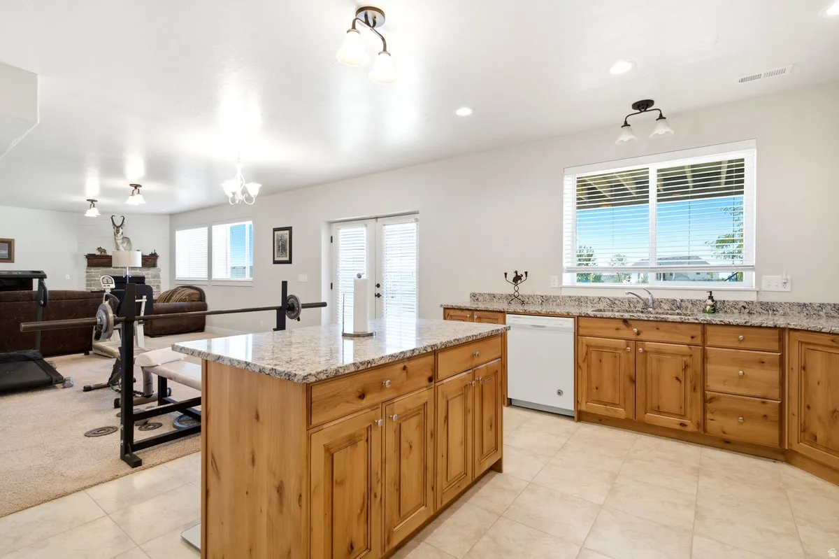 Open-concept space featuring a kitchen island with granite-finish countertop, light wood cabinetry, white tile flooring, and a dishwasher