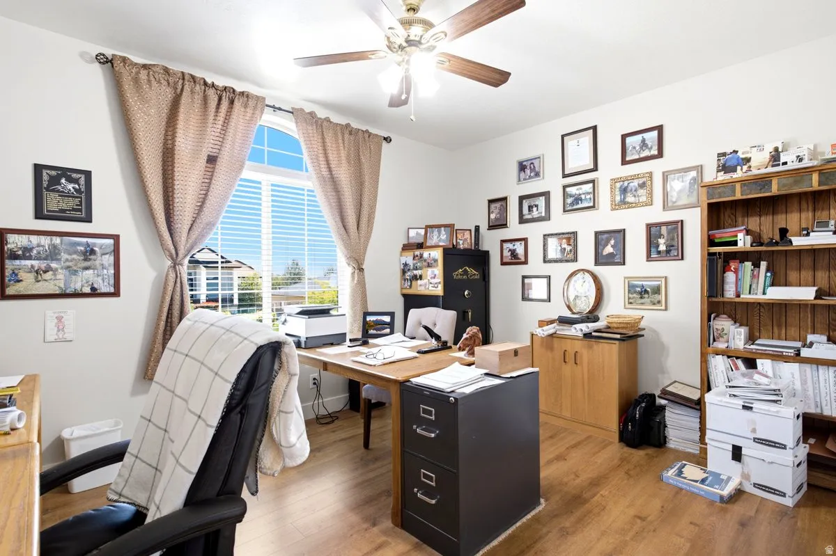 Light-filled interior space featuring wood-finish flooring, a ceiling fan with integrated lighting, and a large arched window with horizontal blinds