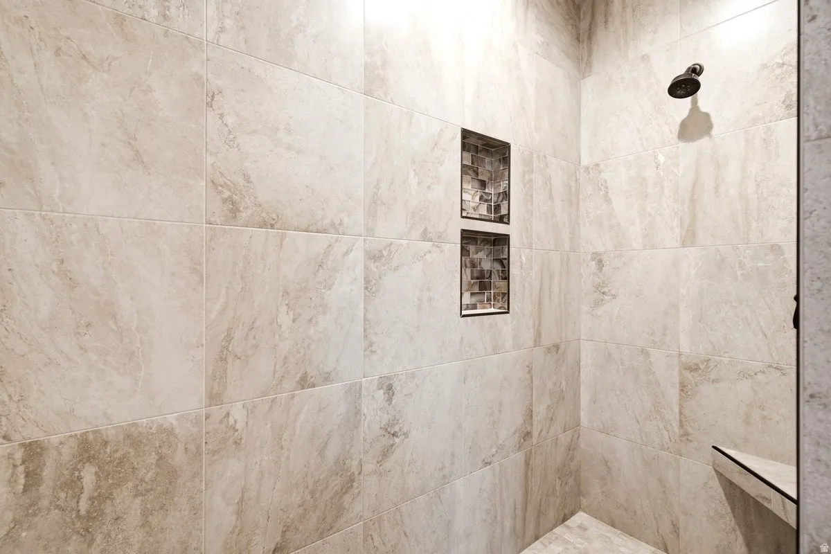 Walk-in shower with large-format beige tiles, two recessed mosaic tile niches, and a corner bench