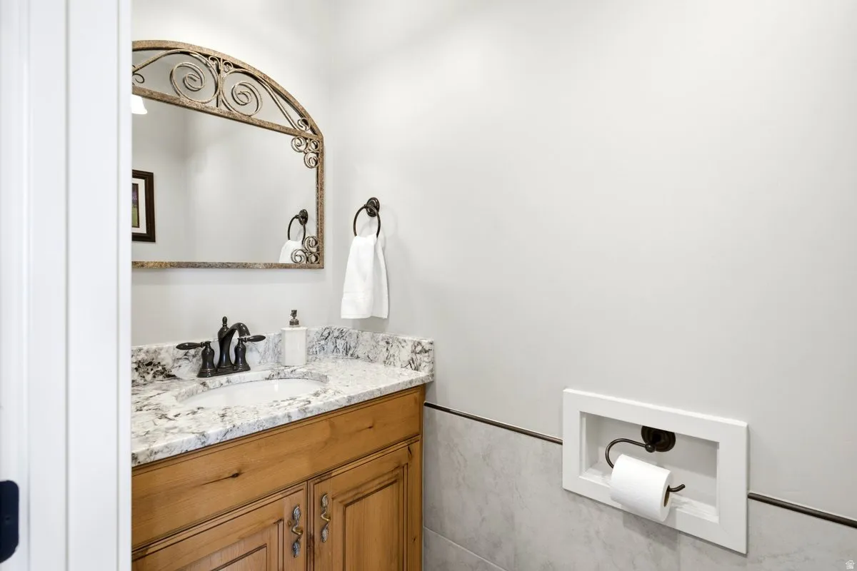 Bathroom featuring a wood vanity with a stone countertop, an undermount sink, and an arched decorative mirror