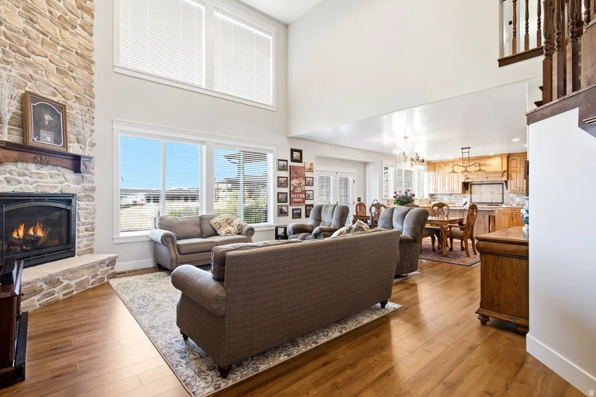 Two-story living area featuring a stone fireplace with wood mantel, large windows with upper transom windows, and wood-finish flooring