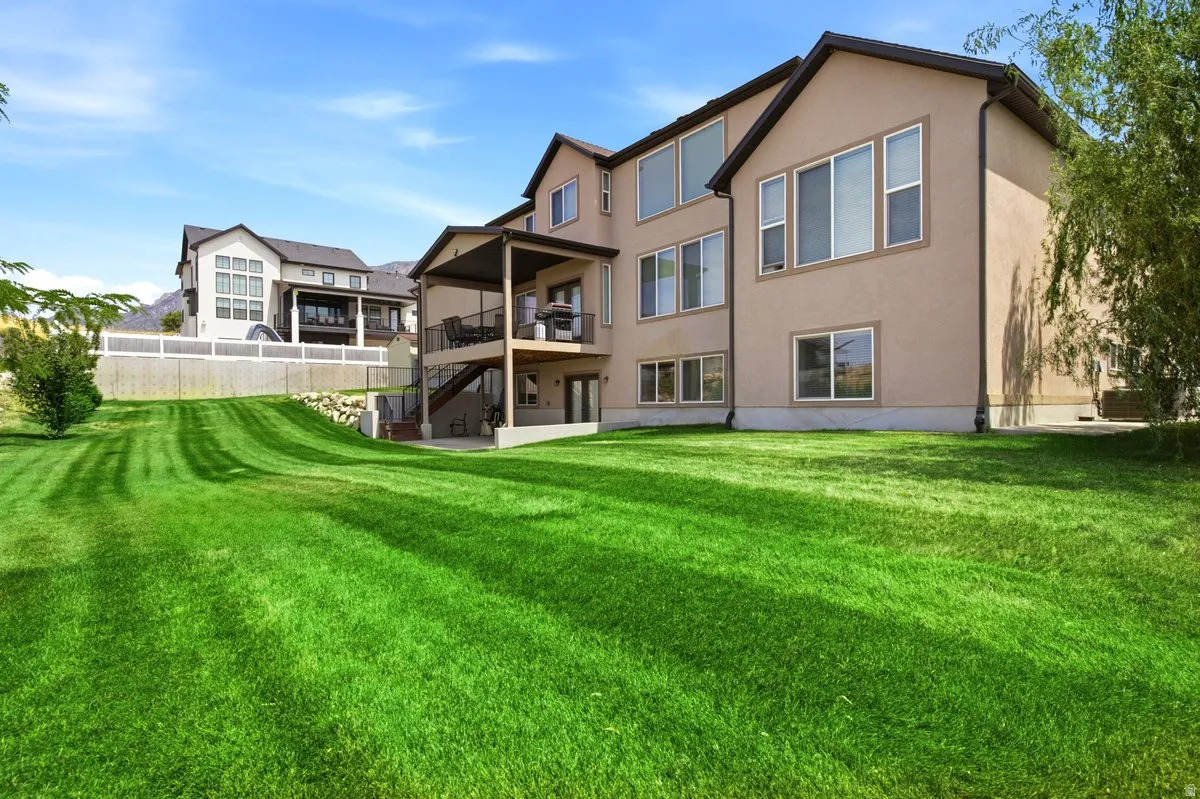 Expansive green lawn with a two-story stucco exterior, covered patio, and upper-level balcony