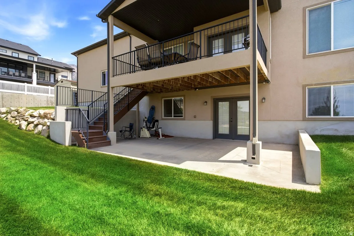 Two-story stucco exterior featuring a ground-level patio, an upper-level balcony with black metal railings, and a walk-out basement with double glass doors