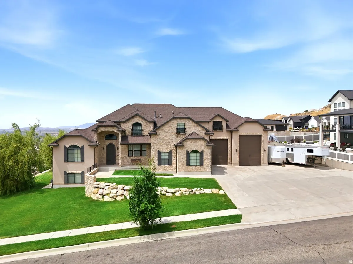 Stately two-story residence featuring a stone and stucco exterior, arched entry, multiple attached garages, and a broad paved driveway