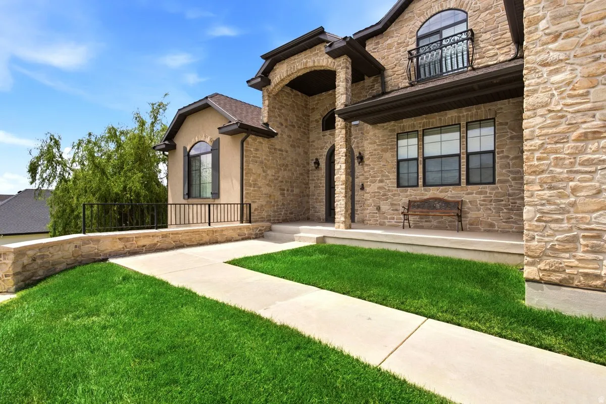 Stone and stucco exterior featuring an arched entryway, covered porch, and second-story Juliet balcony with wrought iron railing
