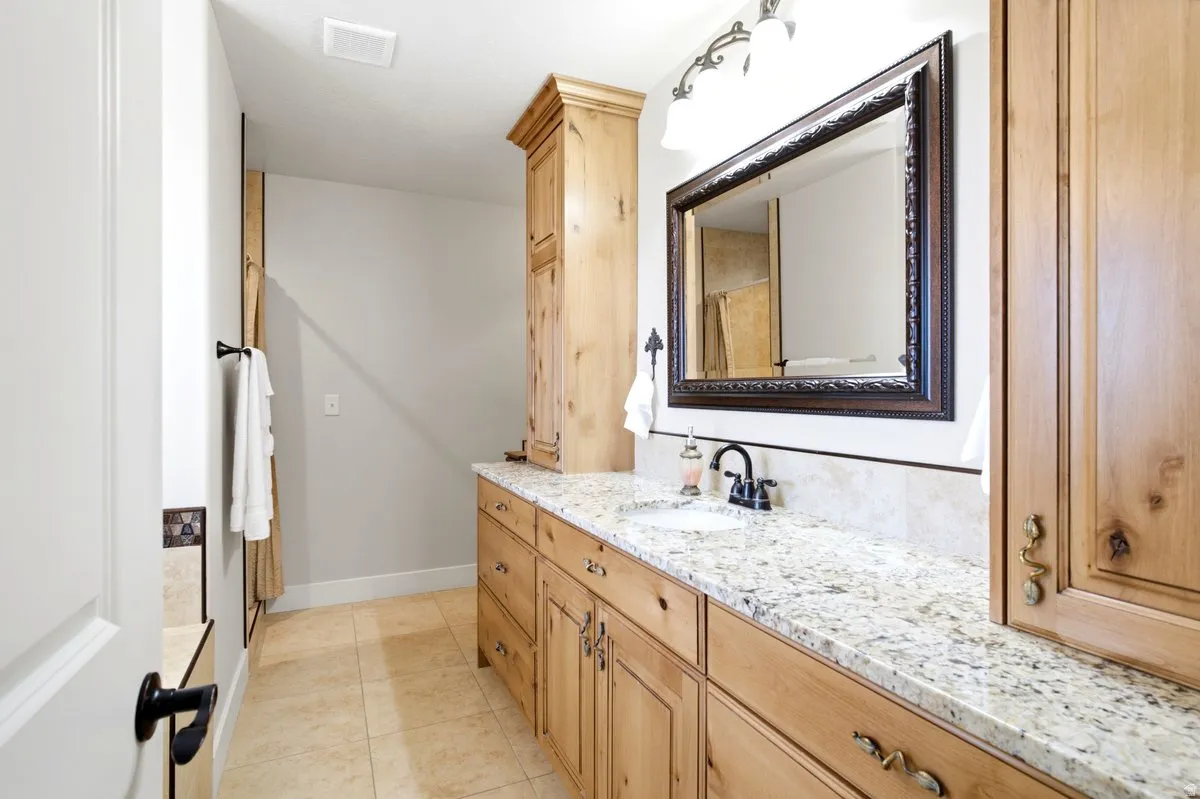 Bathroom vanity featuring light-toned wood cabinetry, a speckled granite countertop, and an undermount sink