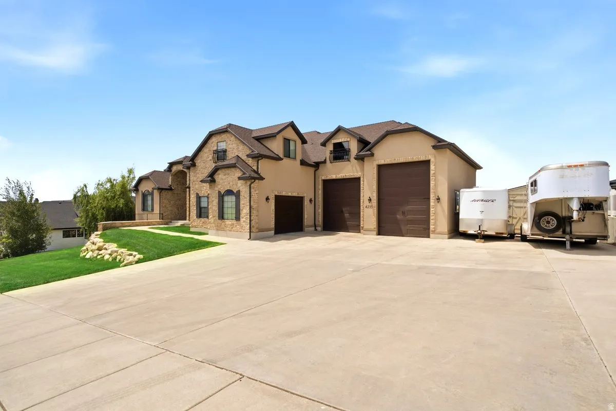 Stucco and stone facade property featuring multiple garage doors, a large paved driveway, and manicured landscaping with natural rock elements