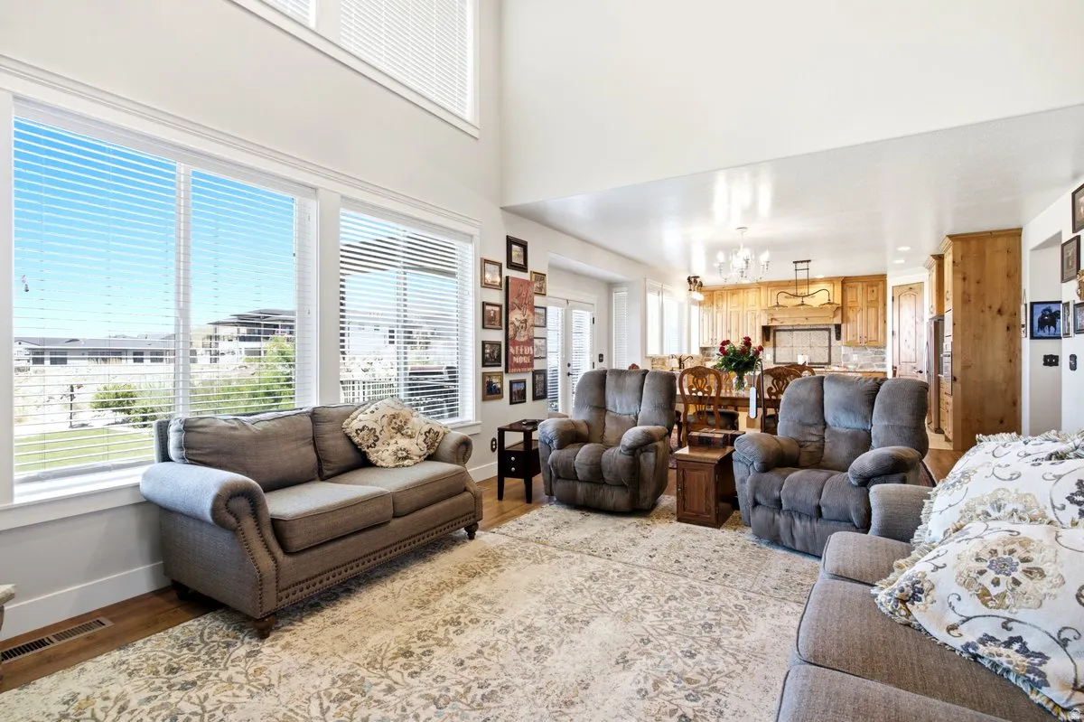 Spacious living area featuring a two-story ceiling, multiple large windows, wood-finish flooring, and an open concept layout connecting to the kitchen and dining area