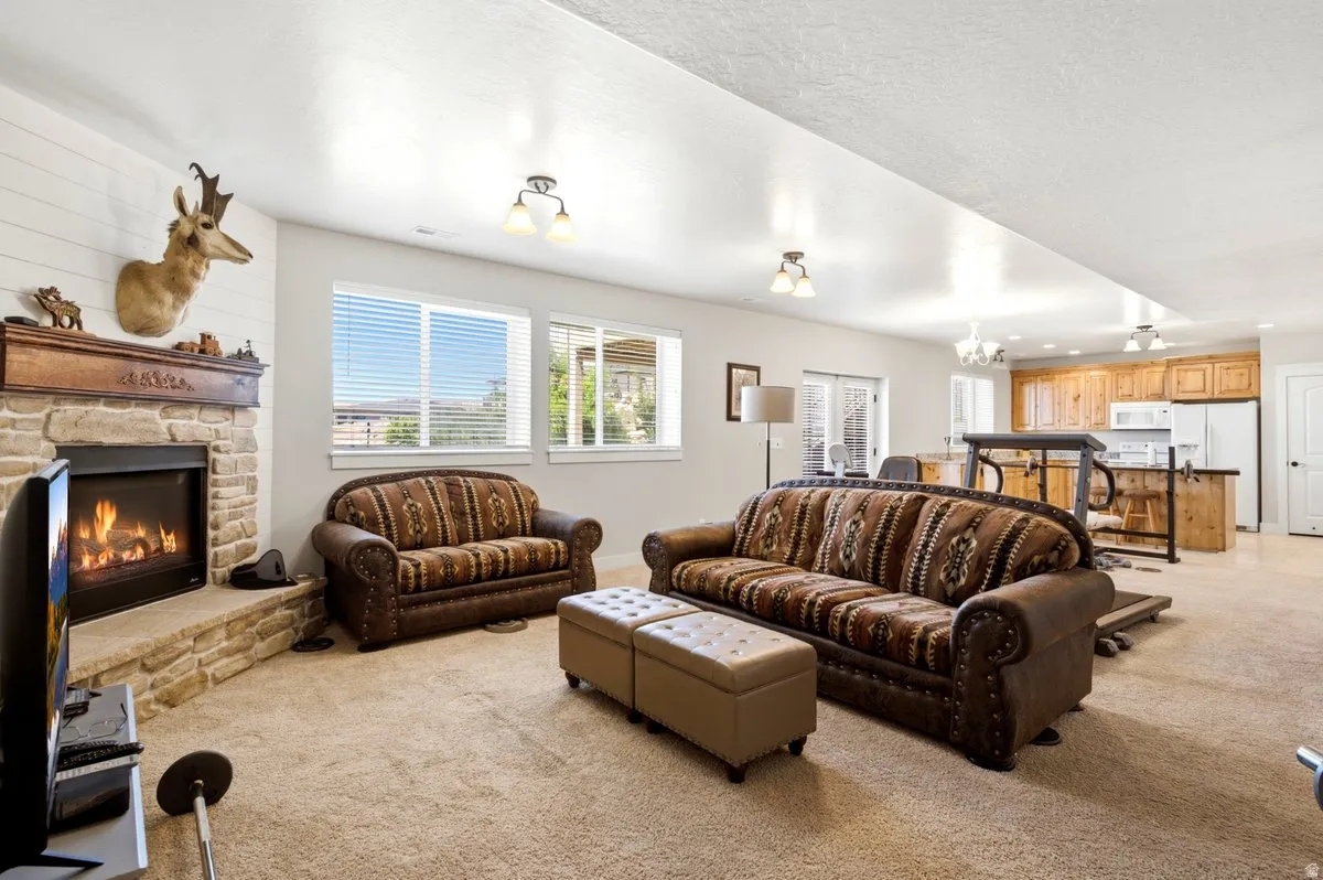Spacious living area featuring a stone fireplace with a wood mantel, light-colored carpeting, multiple windows, and recessed lighting