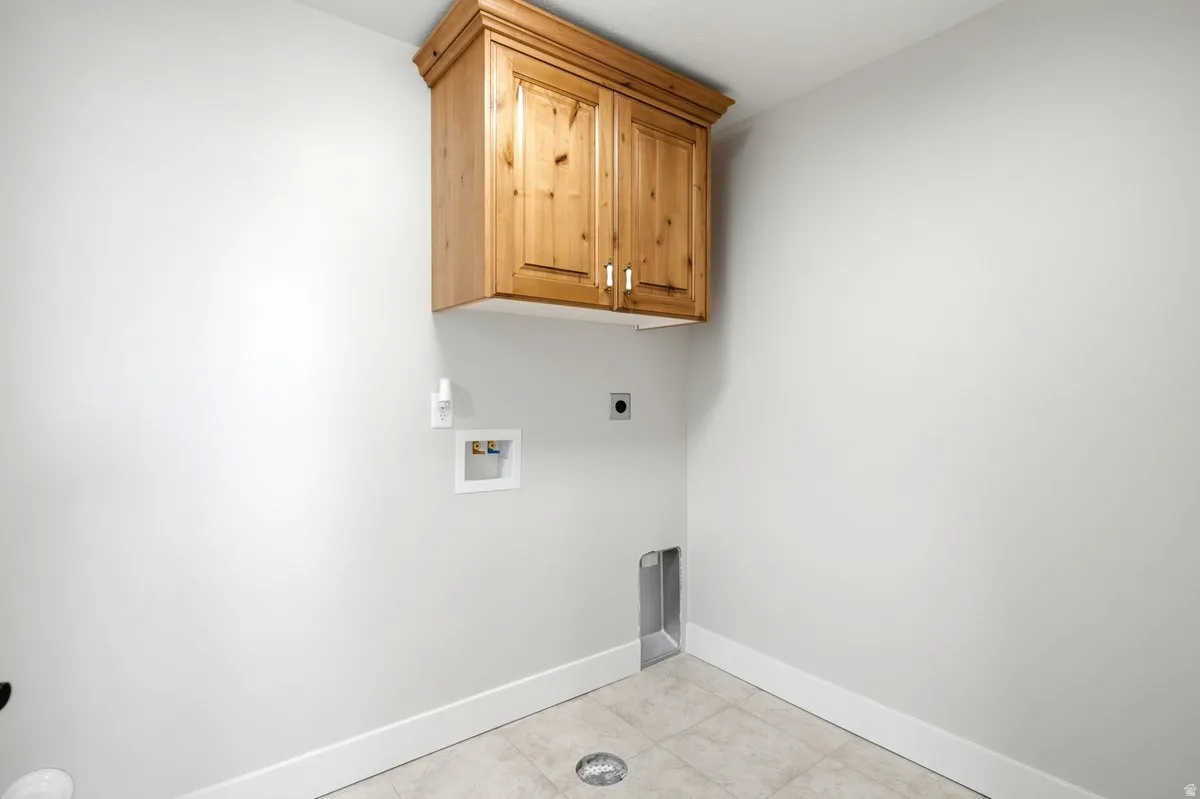 Dedicated laundry space featuring a wood-finish wall cabinet with crown molding, tile flooring, and integrated utility connections