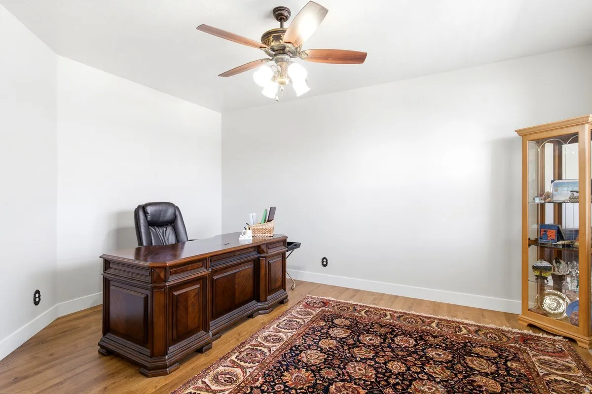 Spacious room featuring wood-finish flooring, white baseboards, and a ceiling fan with integrated lighting