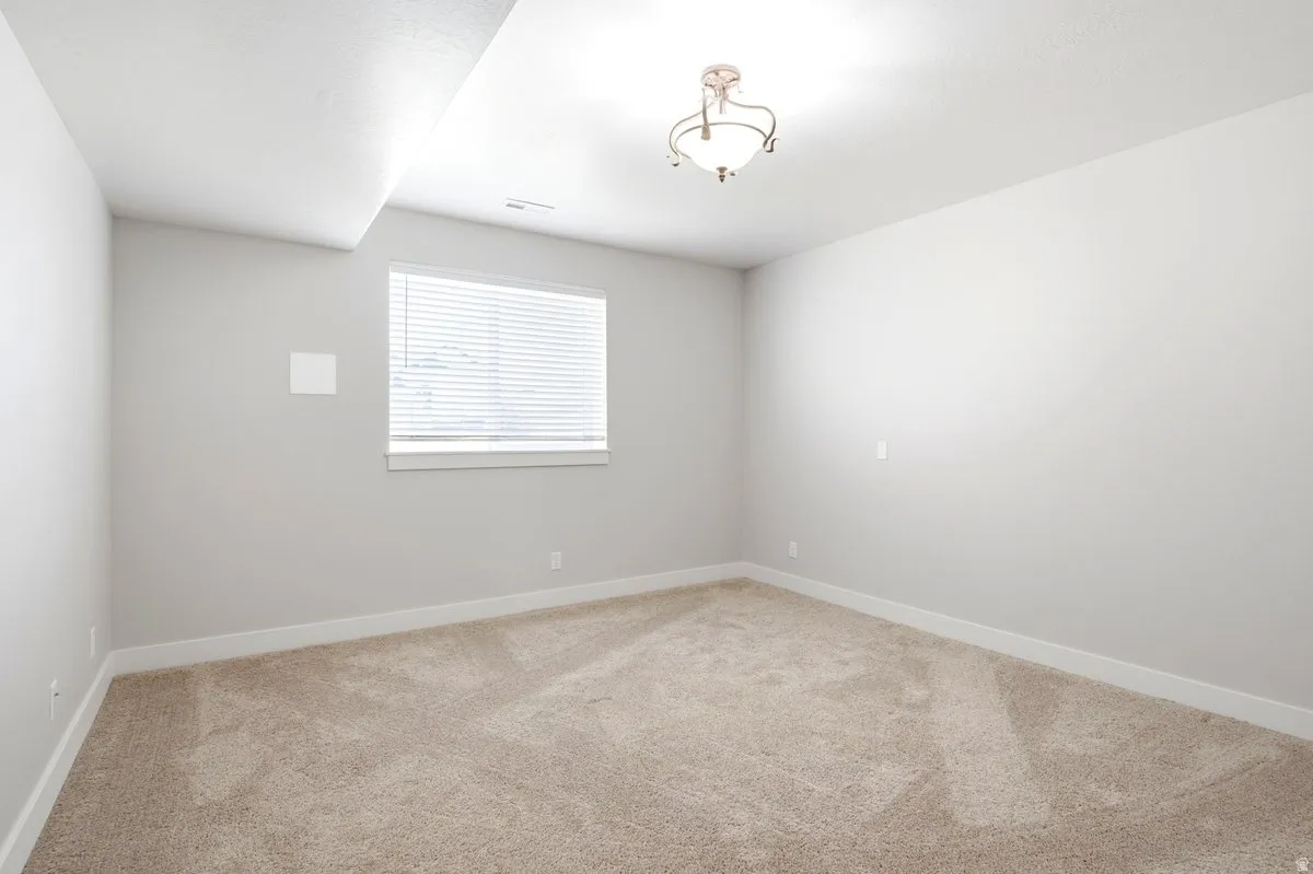 Carpeted room featuring a single window with blinds, a ceiling-mounted light fixture, and white baseboards