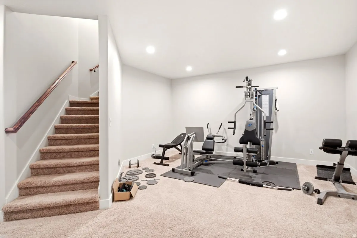 Carpeted staircase with wooden handrail opening to a spacious room featuring recessed lighting and neutral wall tones