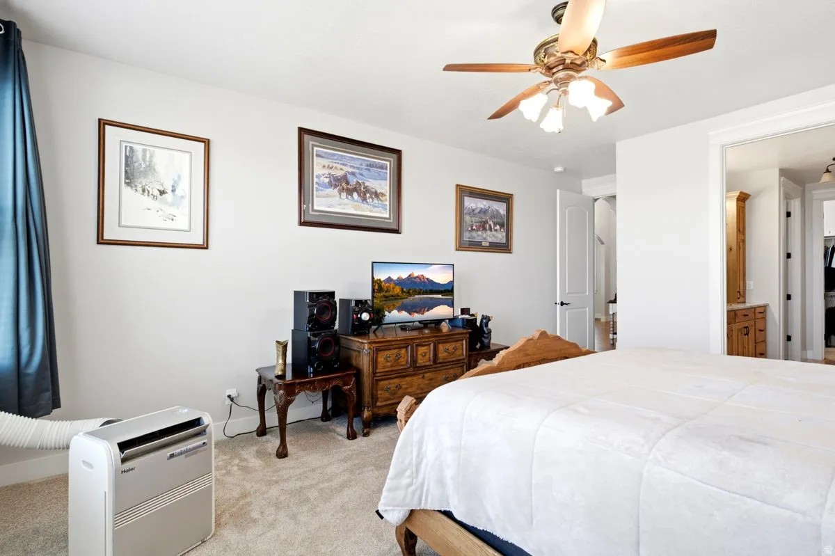 Carpeted bedroom featuring a ceiling fan, light-colored walls, and a doorway leading to an additional space