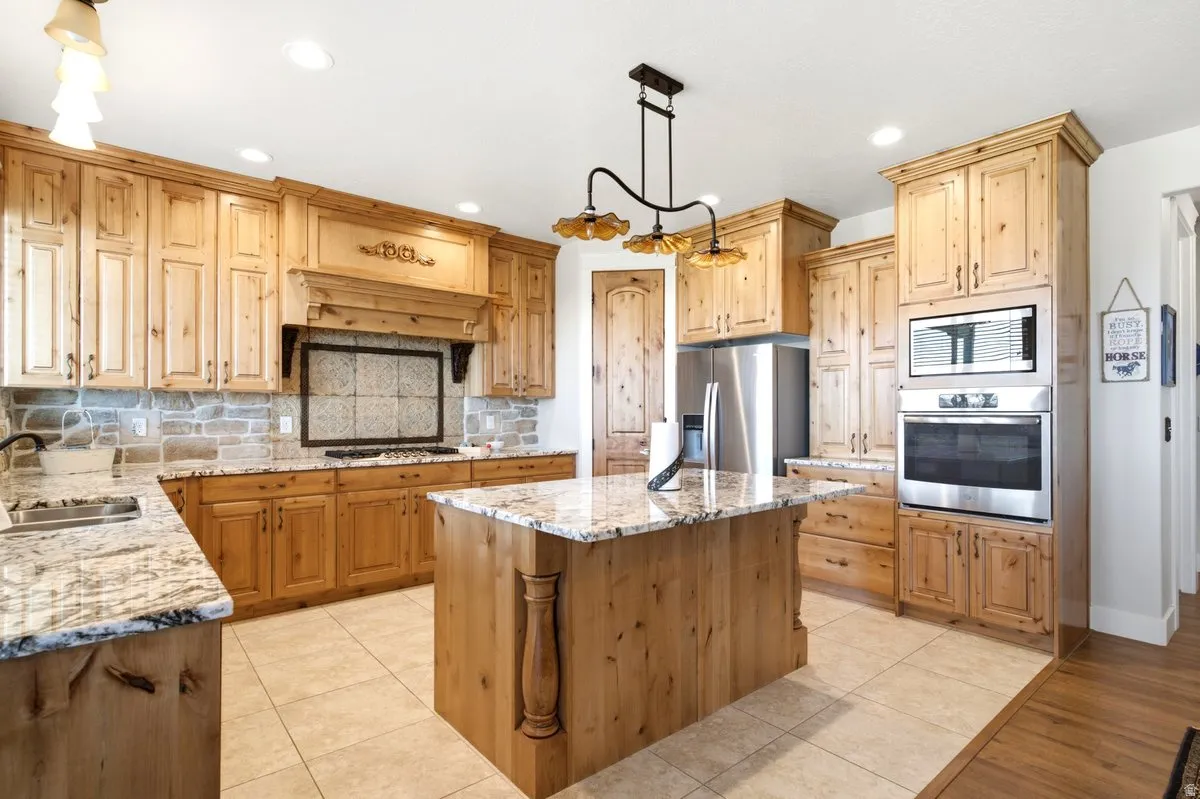 Spacious kitchen featuring extensive light wood cabinetry, stone tile backsplash, granite countertops, and a central island