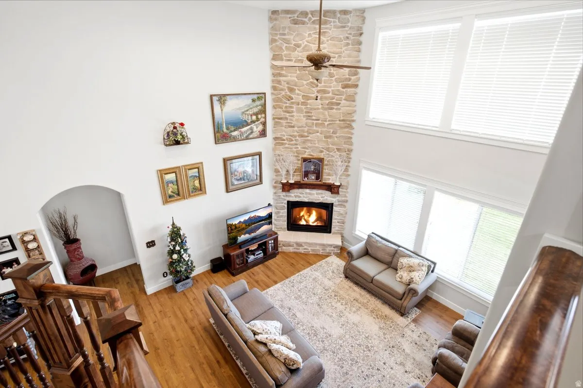 Vaulted ceiling living area featuring a floor-to-ceiling stone-faced fireplace with wood mantel, a ceiling fan, wood-finish flooring, and multiple large windows