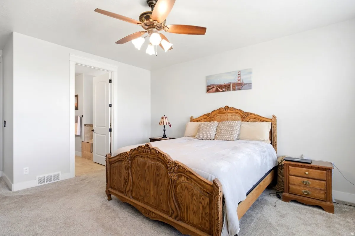 Carpeted room with a ceiling fan light fixture, white walls, and a doorway opening to a bathroom with tile flooring