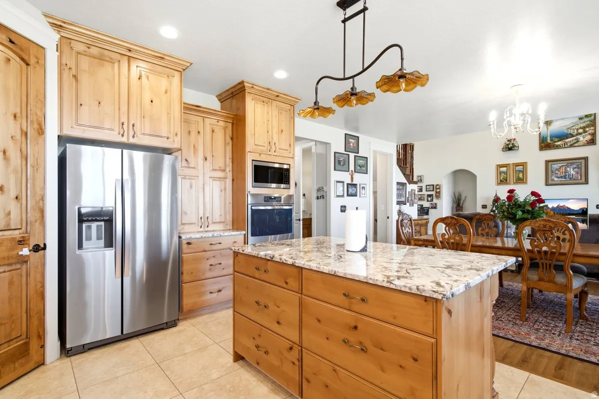 Kitchen featuring light wood cabinetry with crown molding, stainless steel appliances, a built-in oven and microwave, and a granite-topped island