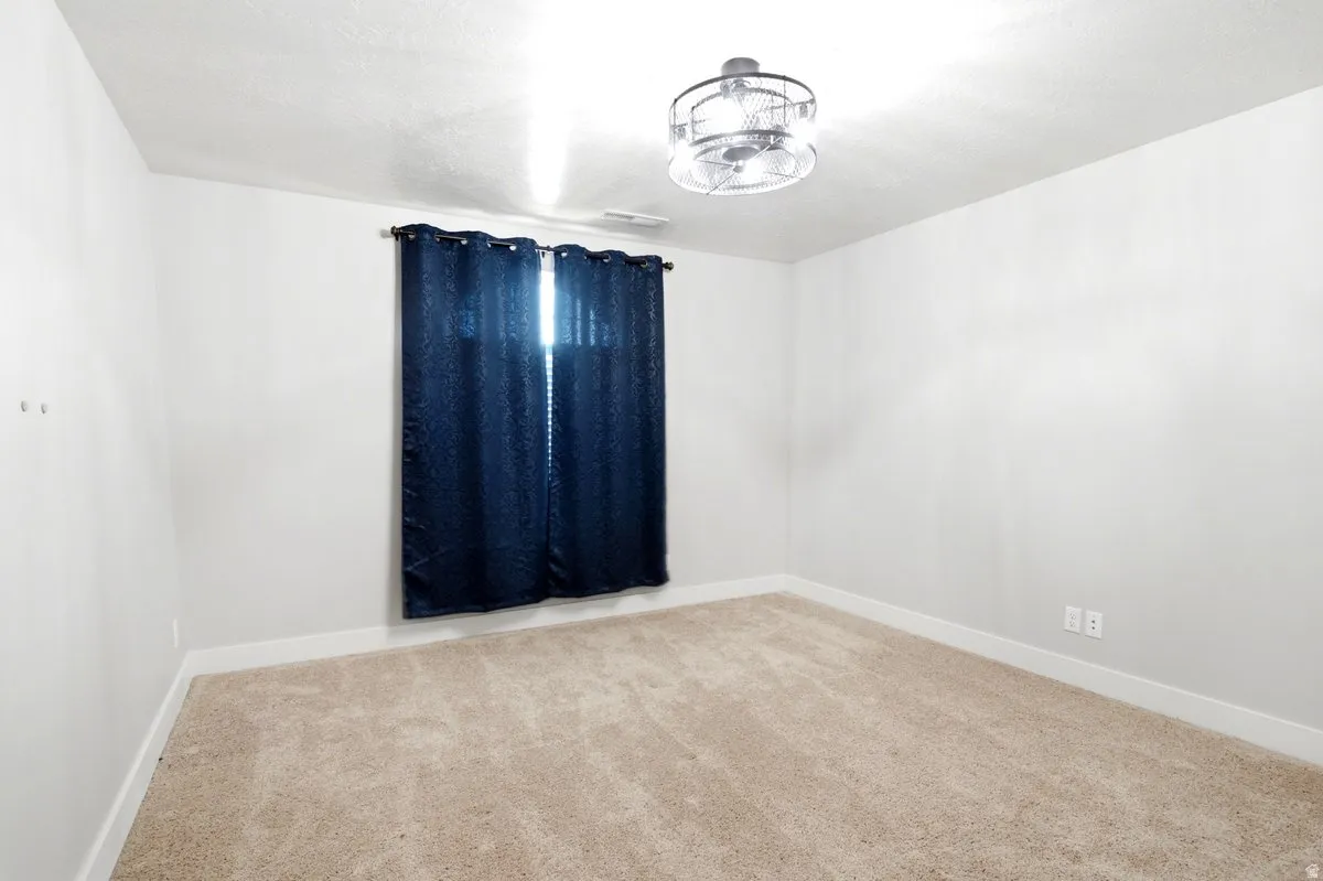 Neutral-toned room featuring a window with dark curtains, light-colored carpeting, white baseboards, and a contemporary ceiling fan