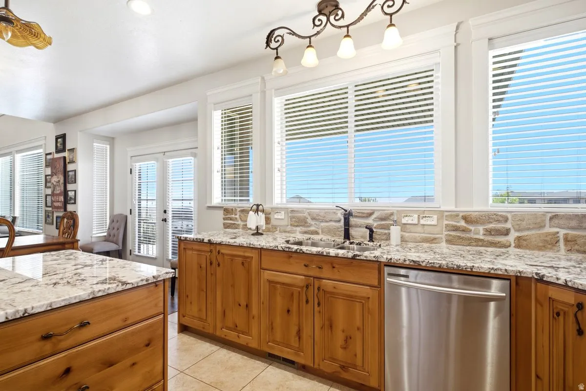 Kitchen featuring a stainless steel dishwasher, light wood cabinetry, stone backsplash, and granite countertops