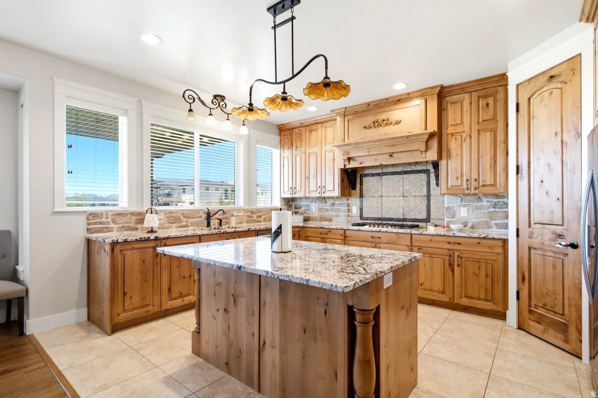 Kitchen featuring extensive wood cabinetry, granite countertops, tile flooring, stone backsplash, and a central island
